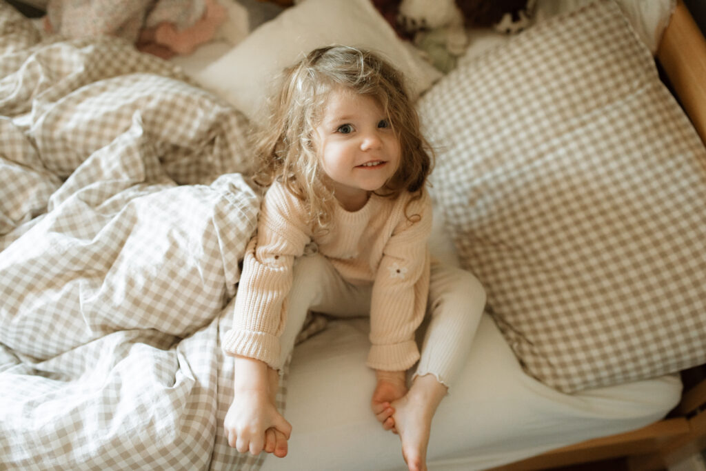 Toddler girl plays in her bed as an example of winter family photo outfits