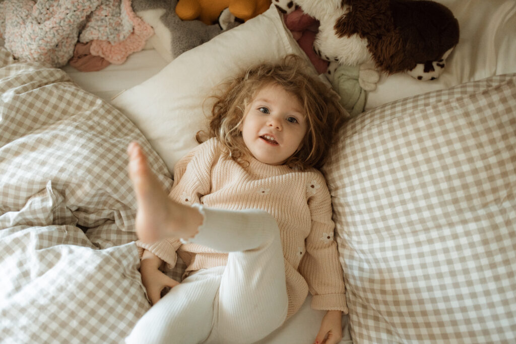 Toddler girl plays in her bed as an example of winter family photo outfits