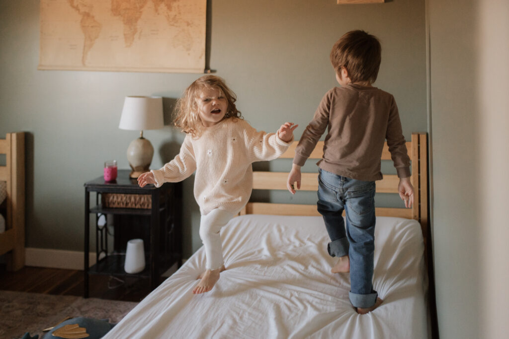 Toddler girl and boy jump on the bed an example of winter family photo outfits