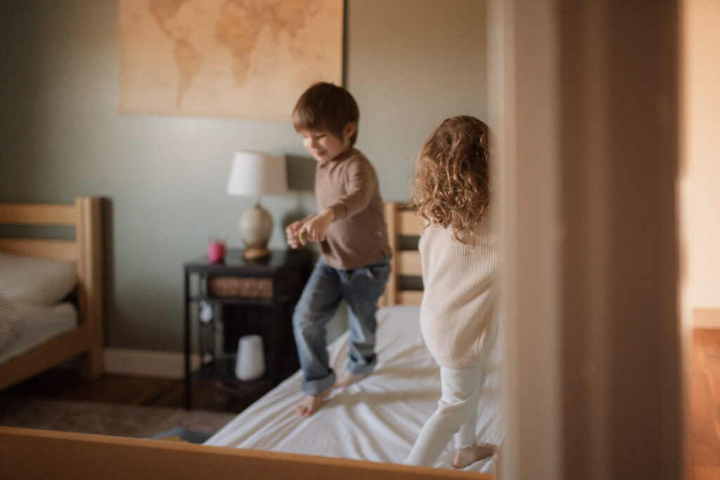 Kids play in neutral colored outfits  on the bed as an example of what to wear for family photos at home