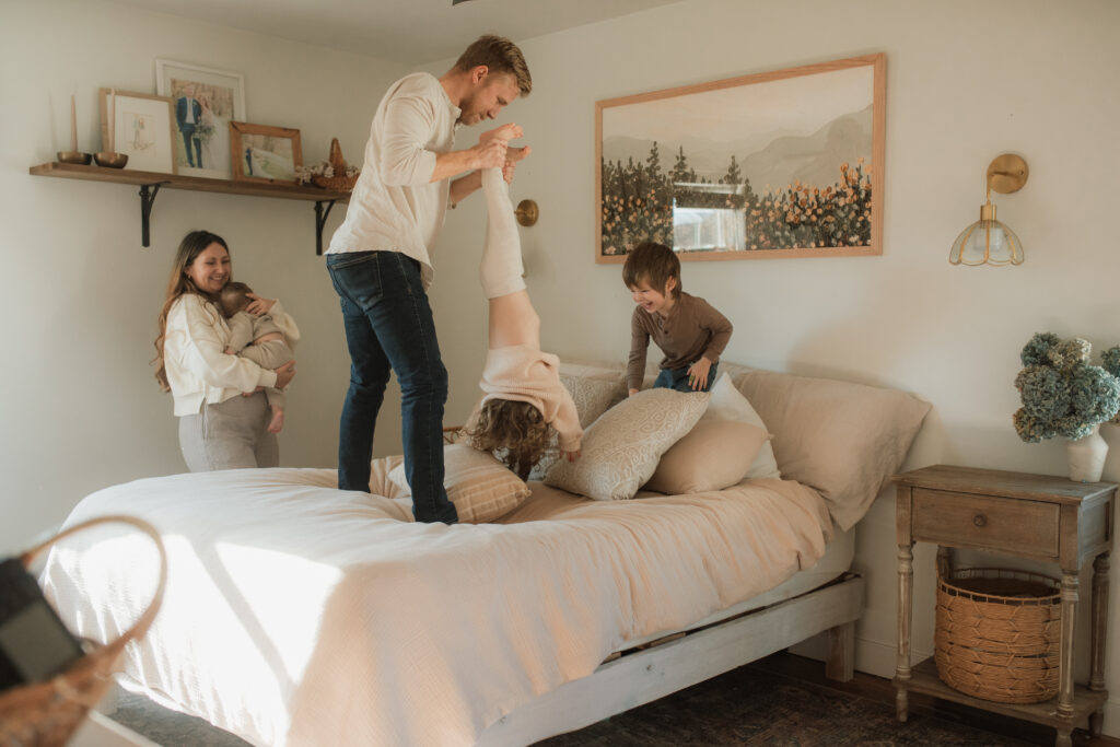 Family in neutral outfits plays on the bed as an example of winter family photo outfits