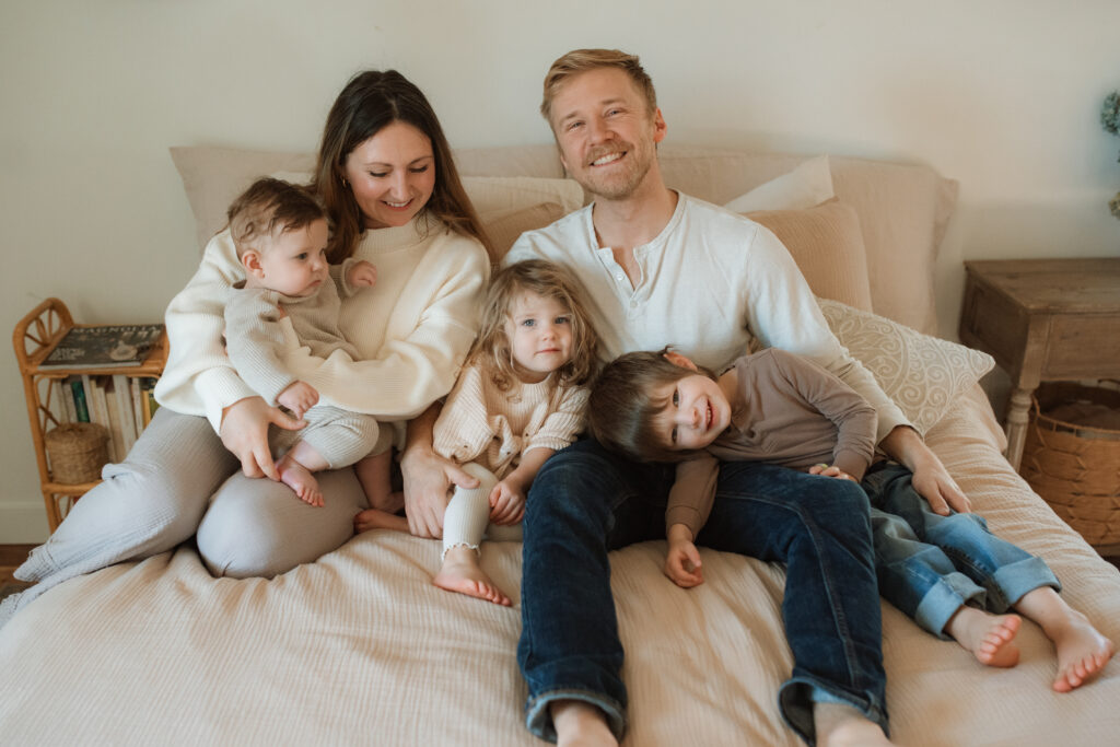 Family in neutral outfits plays on the bed as an example of winter family photo outfits