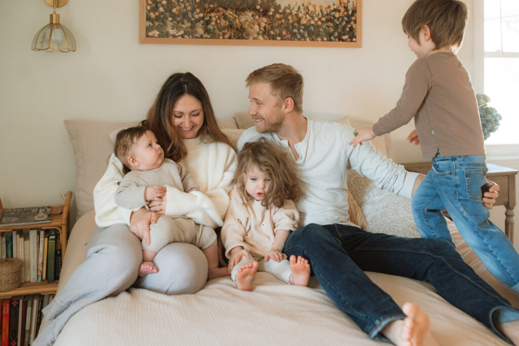 Family in neutral outfits plays on the bed as an example of winter family photo outfits