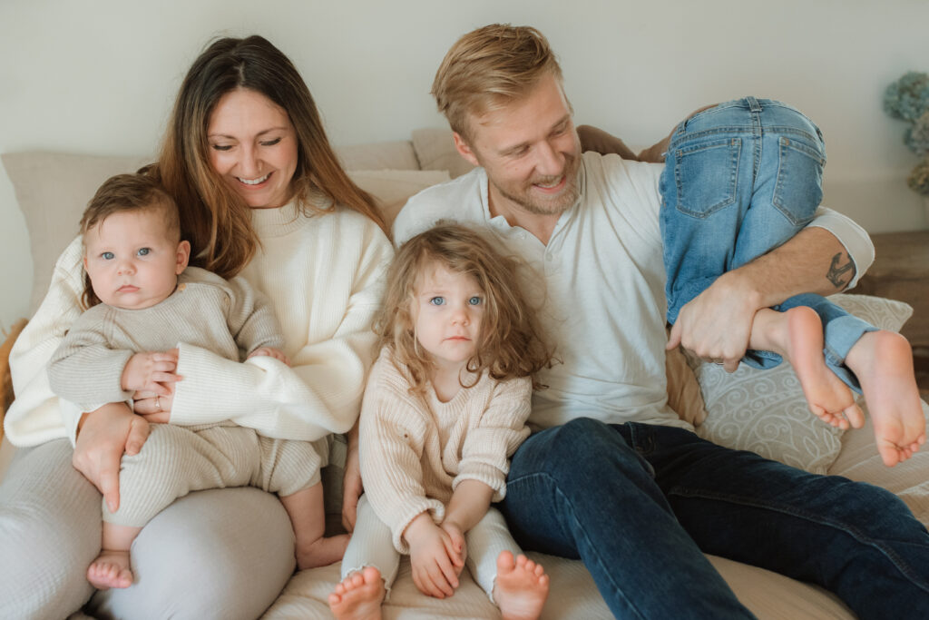 Family in neutral outfits plays on the bed as an example of winter family photo outfits