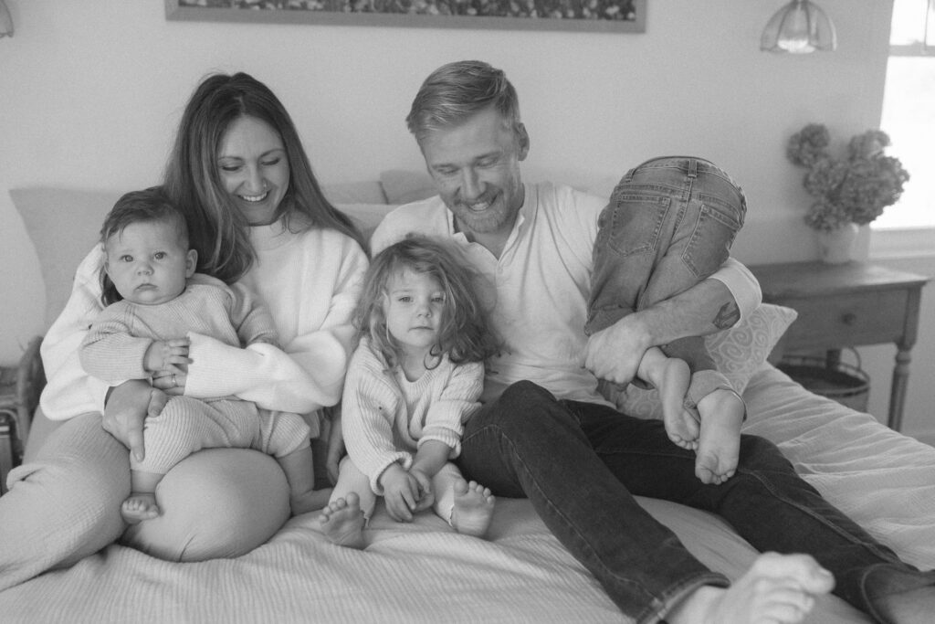 Family in neutral outfits plays on the bed as an example of winter family photo outfits