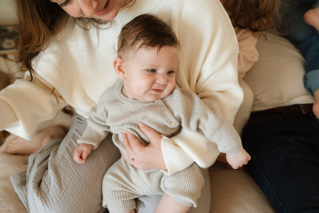 Family in neutral outfits plays on the bed as an example of winter family photo outfits