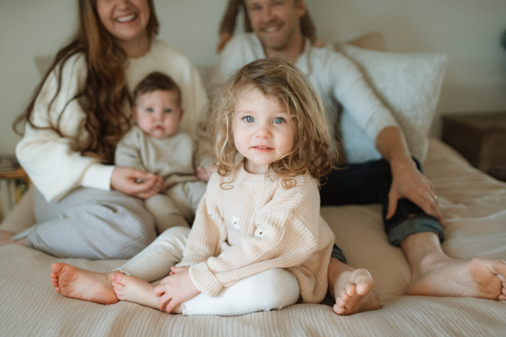 Family in neutral outfits plays on the bed as an example of winter family photo outfits