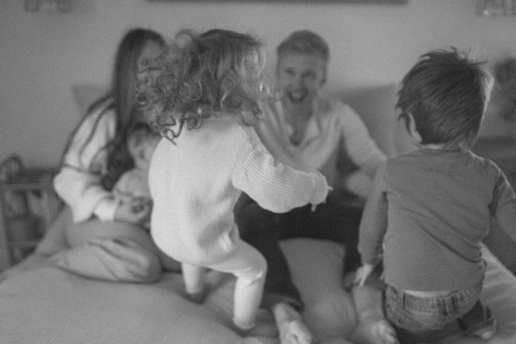 Family in neutral outfits plays on the bed as an example of winter family photo outfits