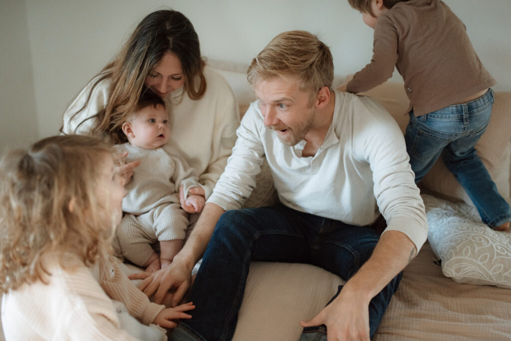 Family in neutral outfits plays on the bed as an example of winter family photo outfits