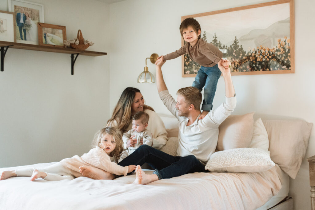 Family in neutral outfits plays on the bed as an example of winter family photo outfits