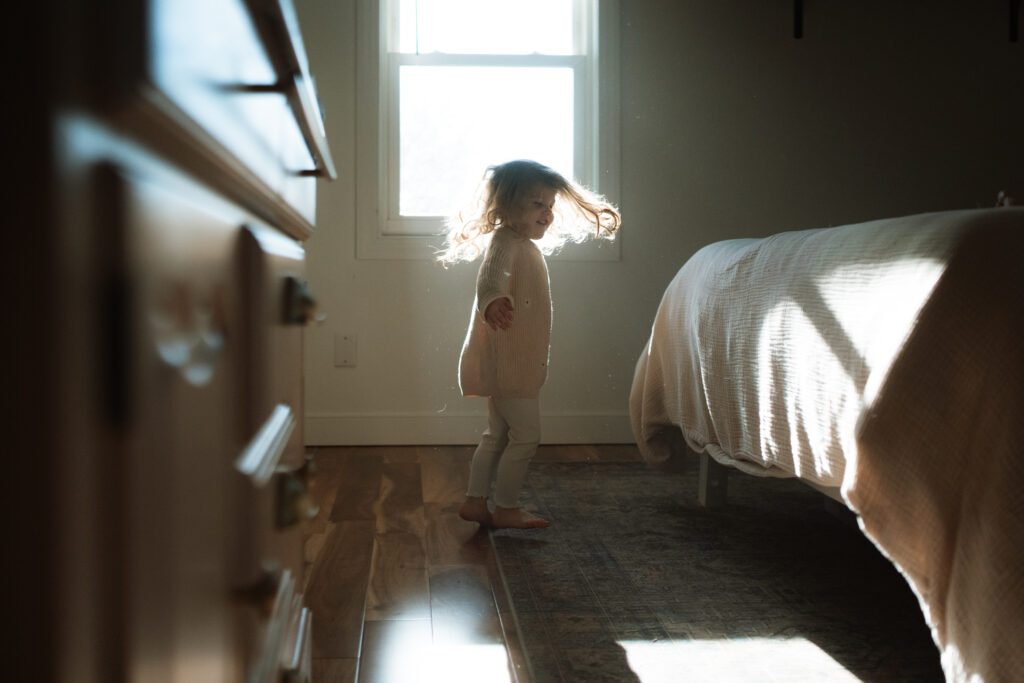 Toddler girl twirls in front of the window as an example of winter family photo outfits