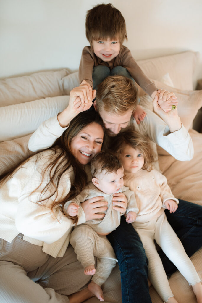 Family in neutral outfits plays on the bed as an example of winter family photo outfits