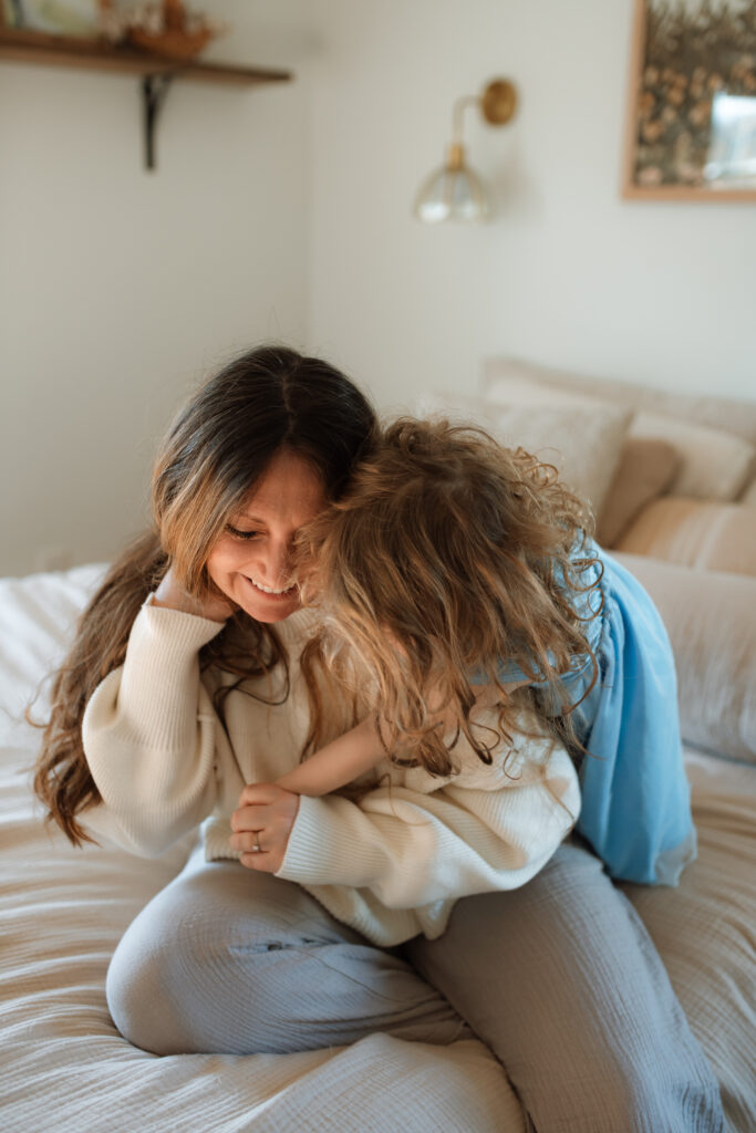 Mom and toddler girl snuggle on the bed as an example of winter family photo outfits