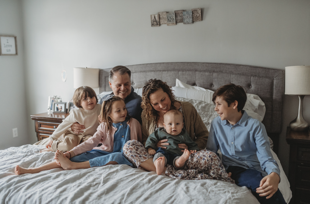 Mom in floral dress snuggles on the bed as an example of what to wear for family photos at home