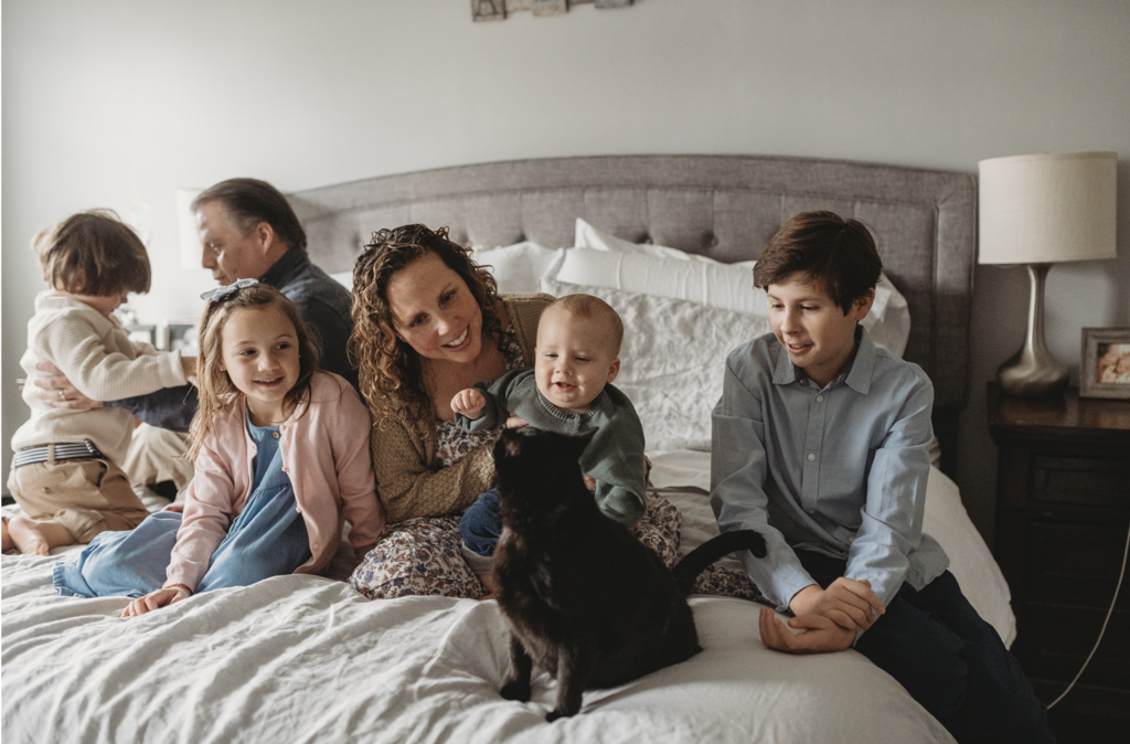 Mom in floral dress snuggles on the bed as an example of what to wear for family photos at home